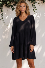 Woman wearing a black dress standing against a white wall with greenery.