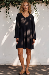 Woman wearing a black dress standing against a white wall with greenery.