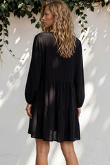 Woman wearing a black dress standing against a white wall with greenery.