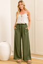 A woman wearing khaki linen pants with an elasticated waist, tie detail, and straight-leg fit, standing in front of a warm beige closet.