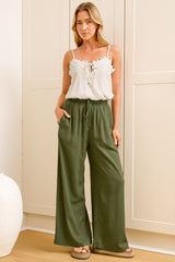 A woman wearing khaki linen pants with an elasticated waist, tie detail, and straight-leg fit, standing in front of a warm beige closet.