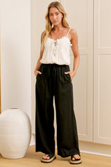 A woman wearing black linen pants with an elasticated waist, tie detail, and straight-leg fit, standing in front of a warm beige closet.