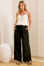A woman wearing black linen pants with an elasticated waist, tie detail, and straight-leg fit, standing in front of a warm beige closet.