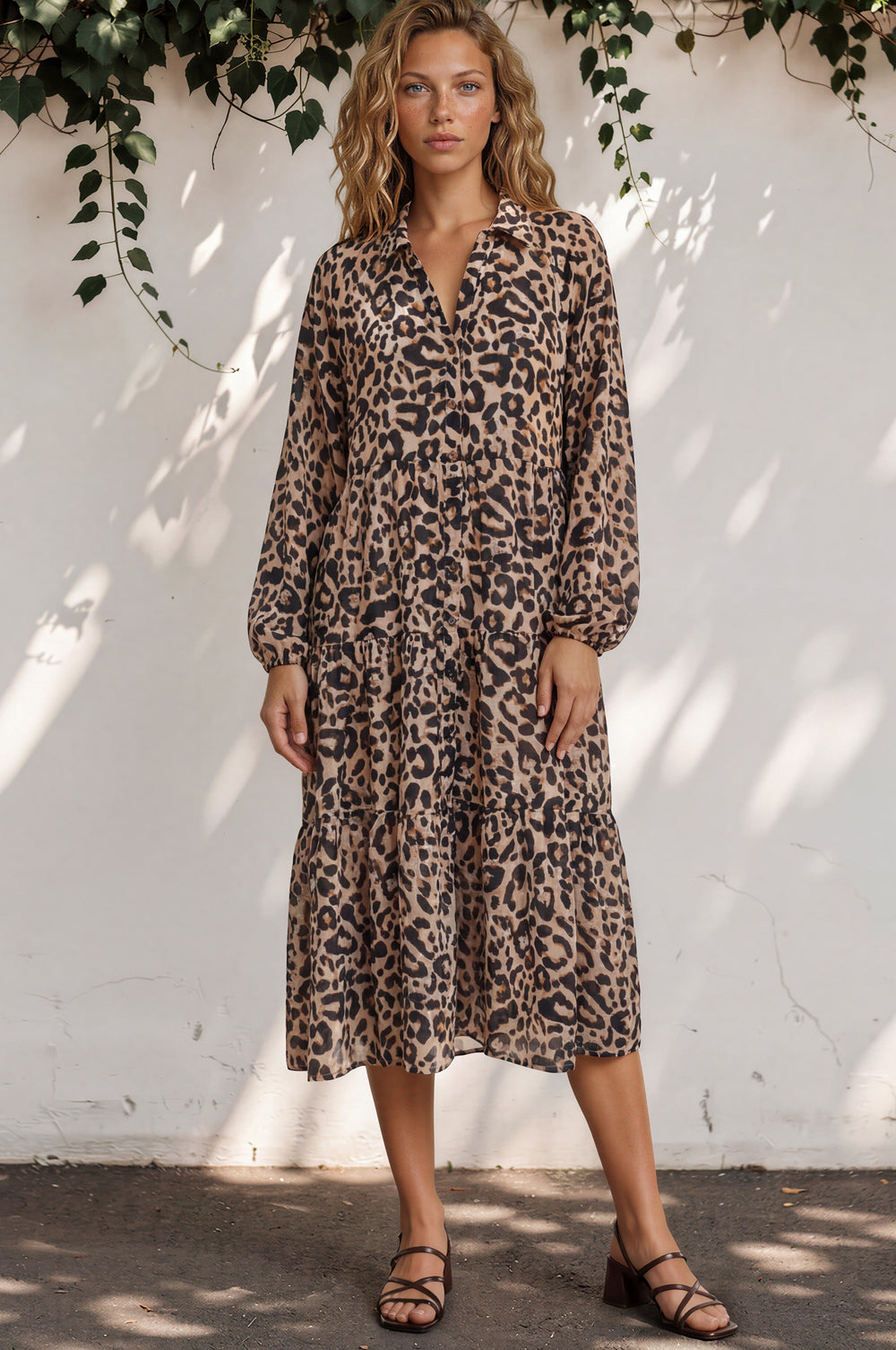 Woman wearing a leopard print dress against a white wall with greenery.