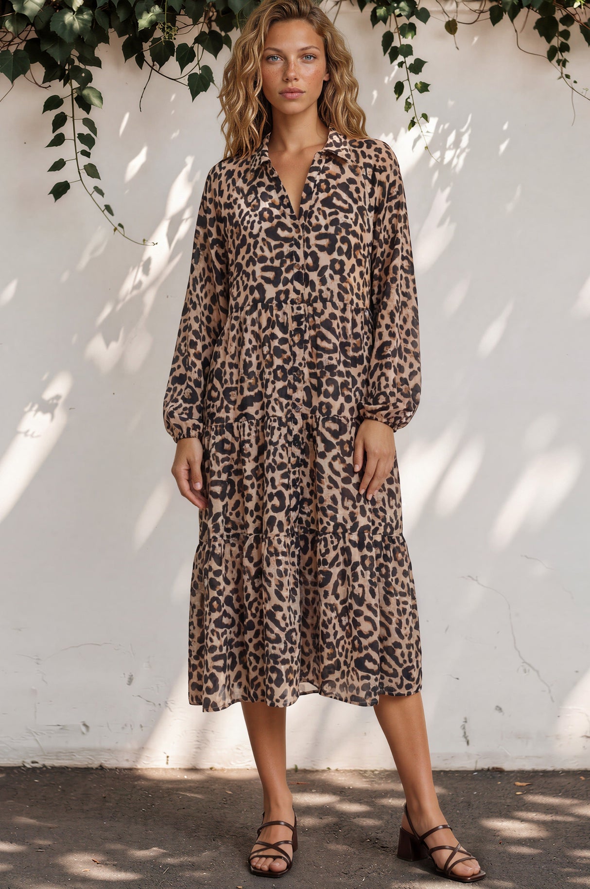 Woman wearing a leopard print dress against a white wall with greenery.