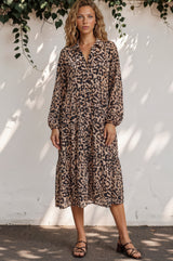 Woman wearing a leopard print dress against a white wall with greenery.
