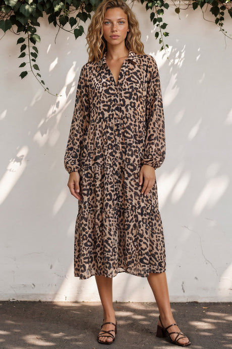 Woman wearing a leopard print dress against a white wall with greenery.