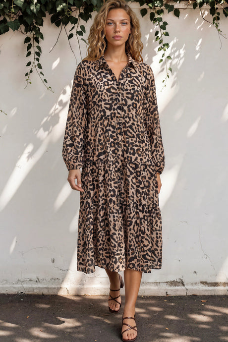 Woman wearing a leopard print dress standing against a white wall with greenery.