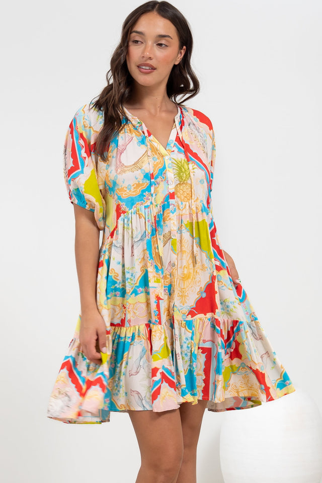 A smiling woman twirling in the Lia Mini Dress in Ecoya Print, a balloon sleeve smock mini dress with a flared tiered skirt in a bright multicoloured abstract print, against a white backdrop