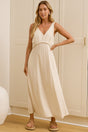 A woman wearing a beige midi dress with a V-neckline, wide straps, braided rope waist detail, and A-line silhouette, standing in front of a warm beige closet.