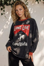 Woman wearing a sweatshirt with 'Long Live Cowgirls' text and design, standing against a white wall with greenery.