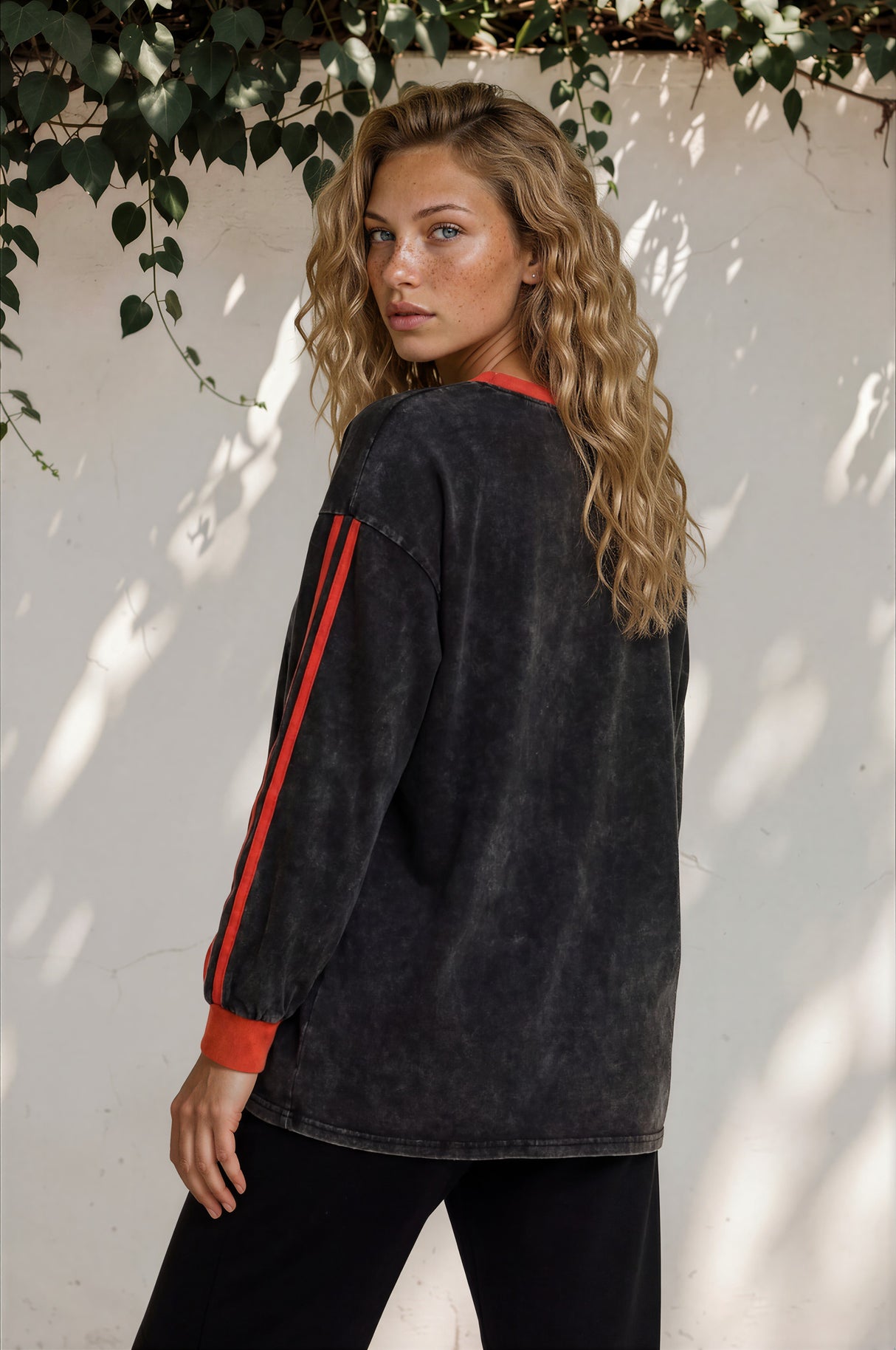 Woman wearing a black jacket with red accents against a white wall with greenery.