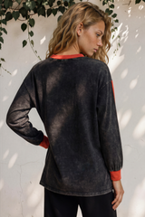 Woman wearing a black long-sleeve top with red accents against a white wall with greenery.
