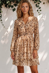 Woman wearing a floral dress standing against a white wall with greenery.