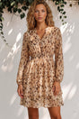 Woman wearing a floral dress standing against a white wall with greenery.