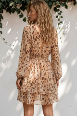Woman wearing a patterned dress standing against a white wall with greenery.
