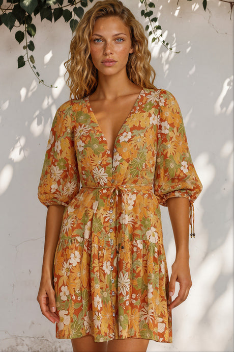 Woman wearing a floral dress with a white wall and greenery in the background