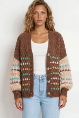 Woman wearing a brown patterned cardigan over a white top and light blue jeans on a white background