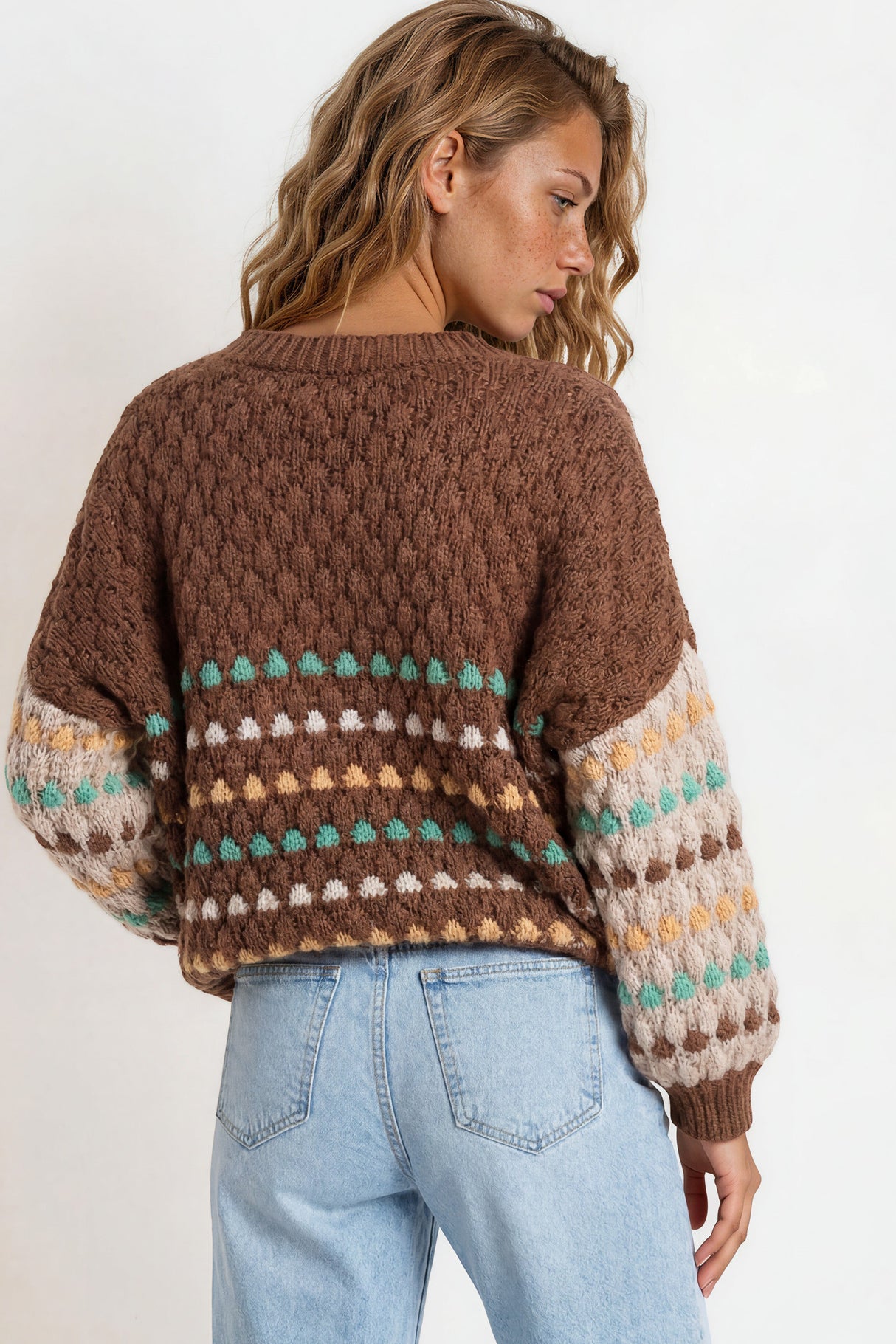 Woman wearing a brown patterned sweater and light blue jeans on a white background