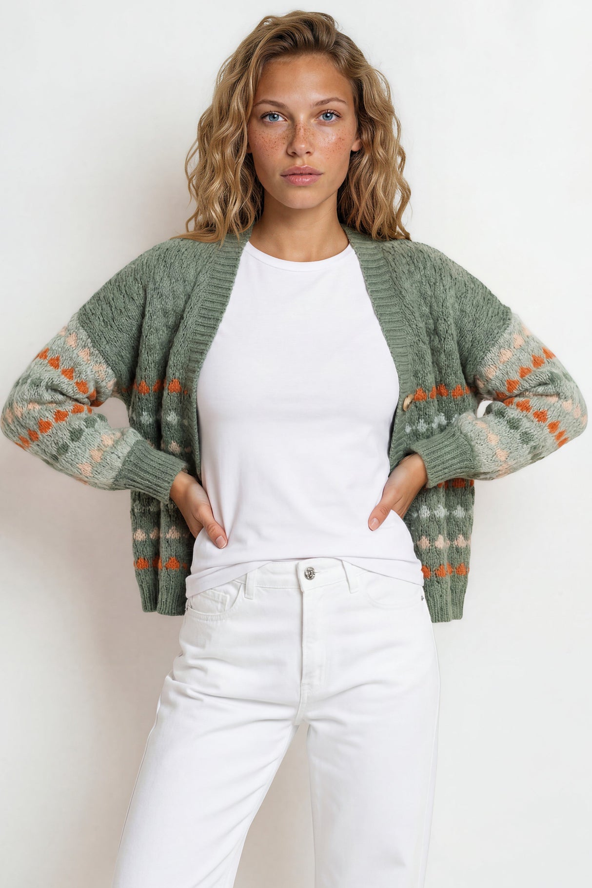 Woman wearing a green patterned cardigan over a white shirt and pants against a plain background