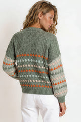 Woman wearing a green sweater with a colorful pattern on a plain background