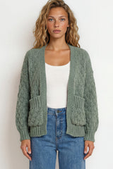 Woman wearing a green cardigan over a white top and blue jeans on a plain background