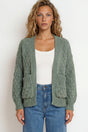 Woman wearing a green cardigan over a white top and blue jeans on a plain background