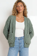Woman wearing a green cardigan, white top, and blue jeans against a white background