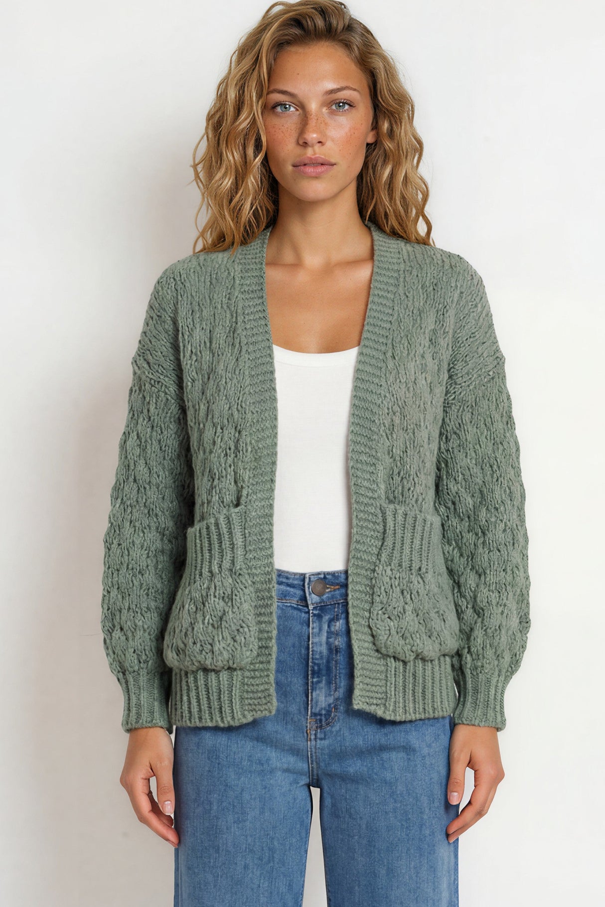 Woman wearing a green knitted cardigan and blue jeans on a white background