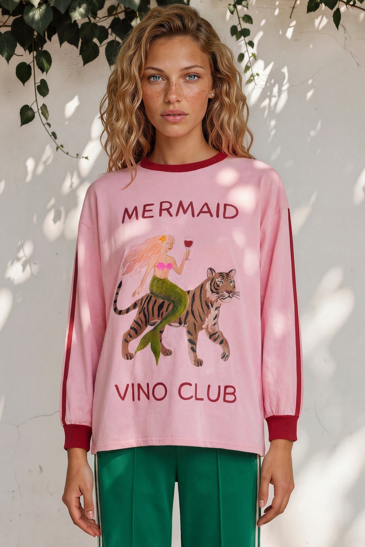 Woman wearing a pink sweatshirt with a mermaid and tiger design and 'Mermaid Vino Club' text.