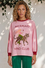 Woman wearing a pink sweatshirt with a mermaid and tiger design and 'Mermaid Vino Club' text.