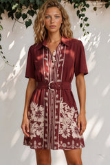 Woman wearing a maroon dress with floral pattern against a white wall.