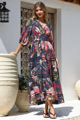 Woman wearing a colourful floral Salty Crush dress standing outdoors near decorative pots.