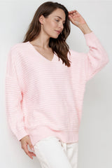 Woman wearing a light pink sweater and white pants against a neutral background