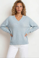 Woman wearing a light blue sweater and white pants against a plain background