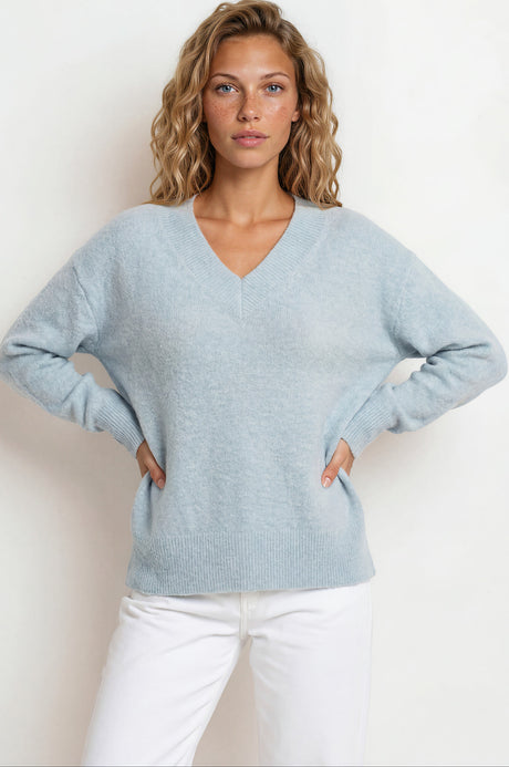 Woman wearing a light blue sweater and white pants against a plain background