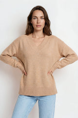 Woman wearing a beige sweater and light blue jeans against a white background