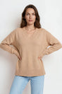 Woman wearing a beige sweater and light blue jeans against a white background