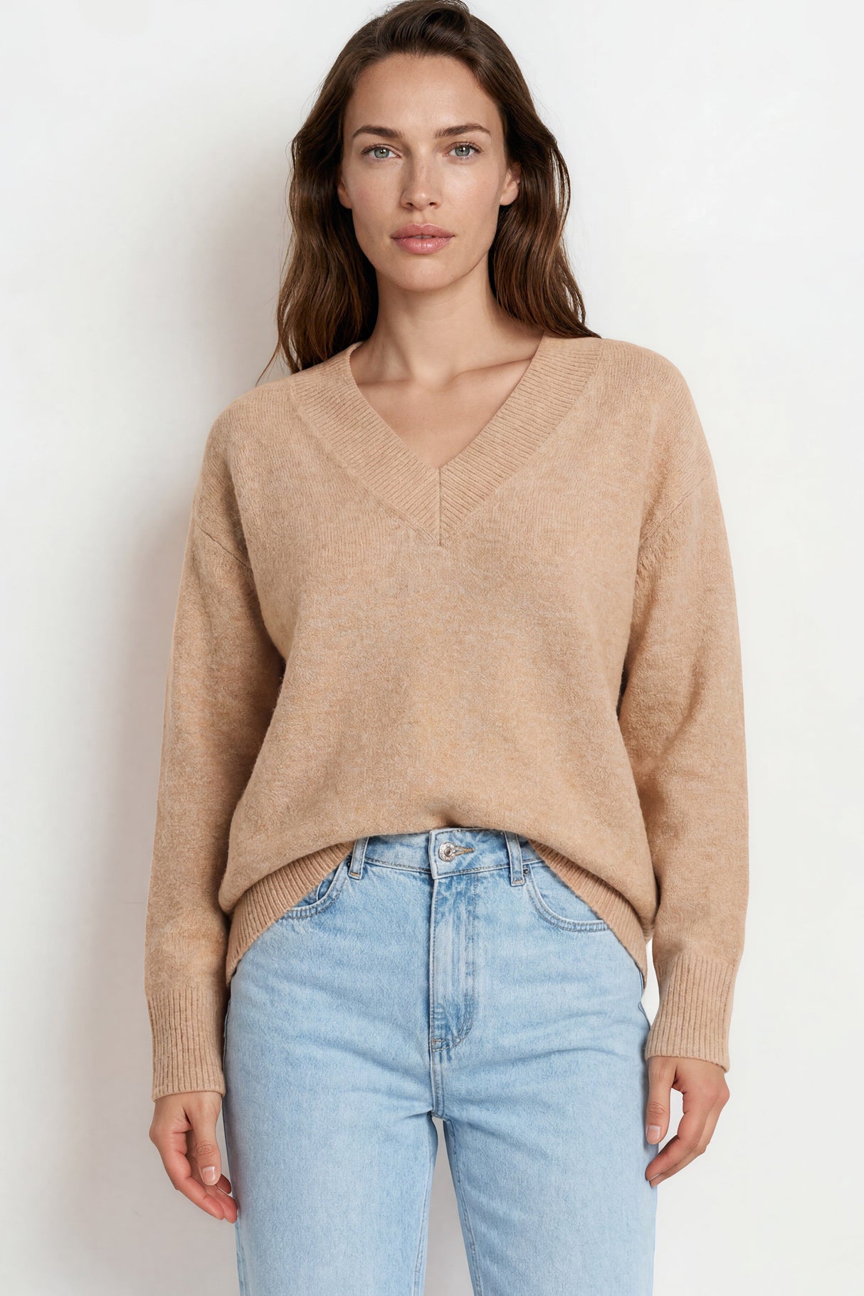 Woman wearing a beige sweater and light blue jeans against a white background