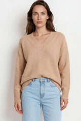 Woman wearing a beige sweater and light blue jeans against a white background