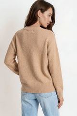 Woman wearing a beige sweater and light blue jeans on a plain background