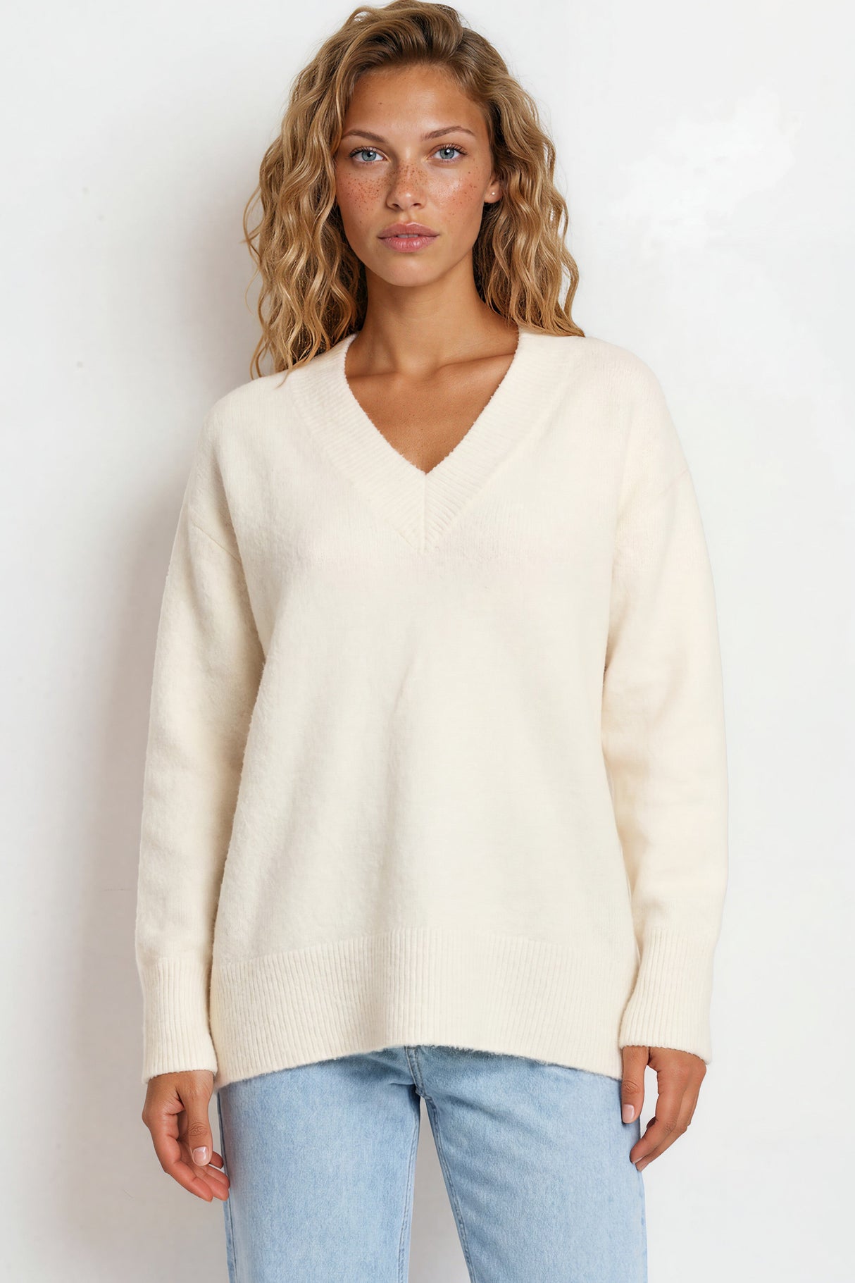 Woman wearing a cream sweater and light blue jeans against a white background