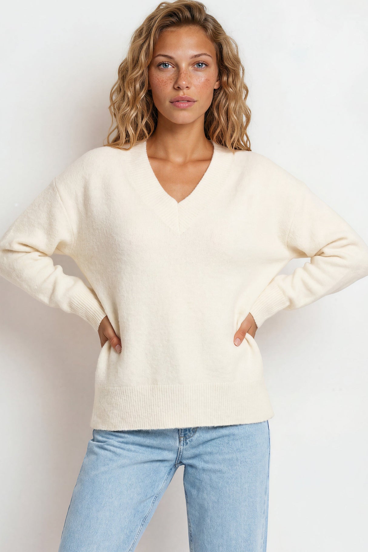 Woman wearing a cream sweater and light blue jeans against a white background