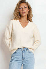 Woman wearing a cream sweater and light blue jeans against a white background
