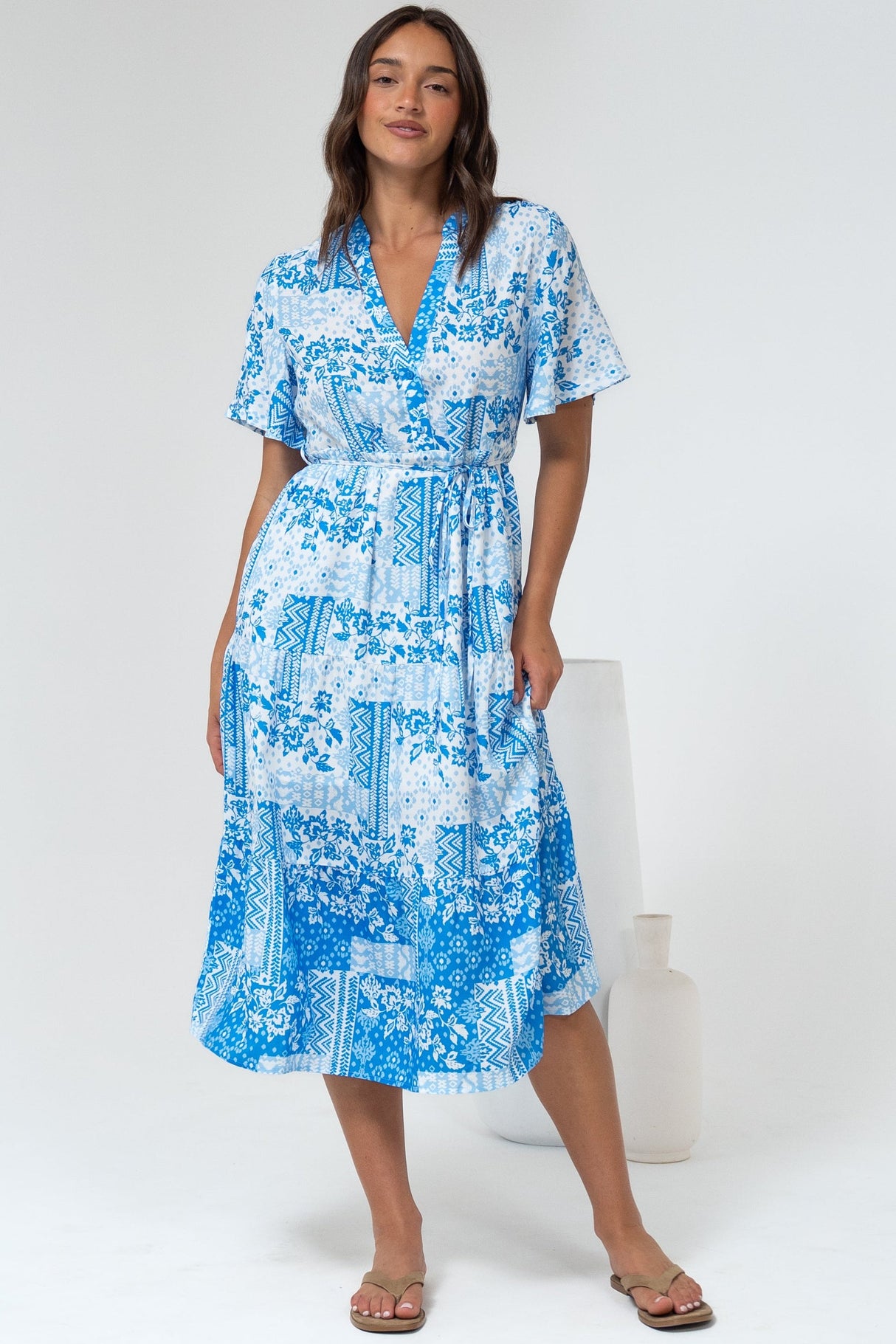Woman wearing a blue floral dress standing in a white room.