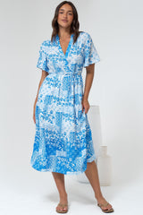Woman wearing a blue floral dress standing in a white room.