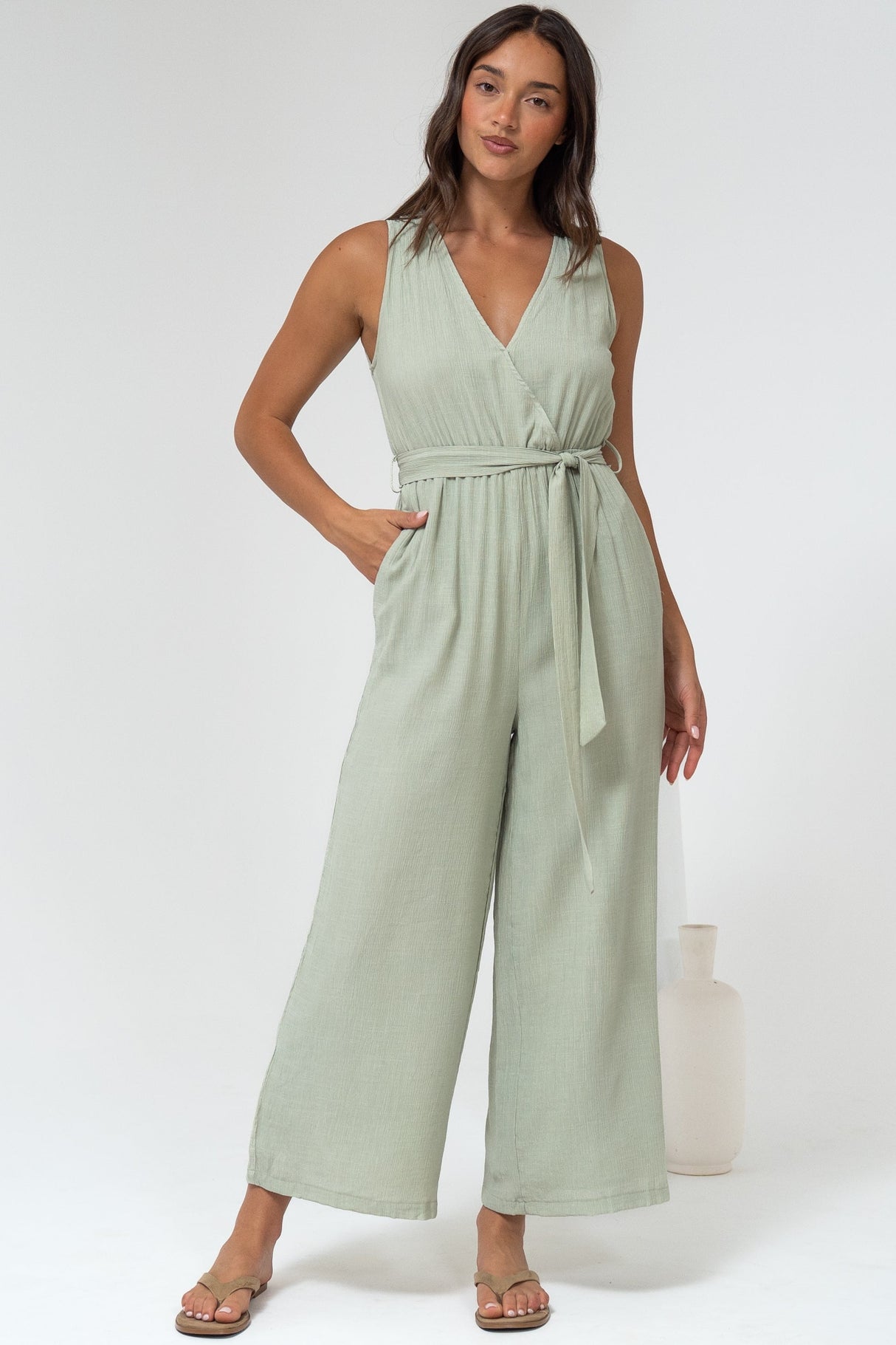 Woman wearing a light green jumpsuit standing against a white background