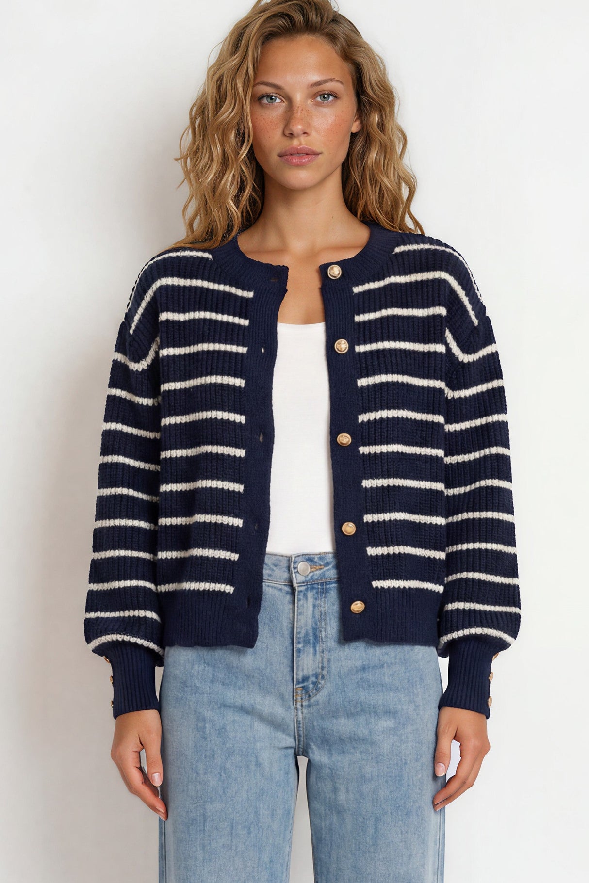 Woman wearing a navy and white striped cardigan with light blue jeans on a white background