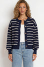 Woman wearing a navy and white striped cardigan with light blue jeans on a white background