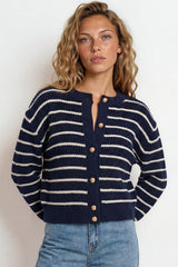 Woman wearing a navy and white striped sweater with blue jeans against a plain background